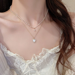 Detailed close-up of double-layered gold necklace with pearl chain and heart shell pendant