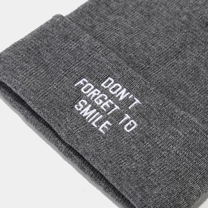 Close-up of grey knitted beanie featuring white 'DON'T FORGET TO SMILE' letter embroidery