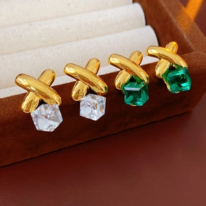 Macro shot of vintage gold X-shaped earrings with clear and green square stones