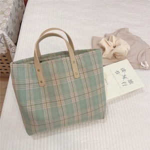 Detail of green plaid tote bag featuring brown leather handles with rivet reinforcement
