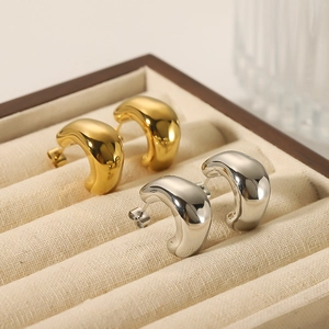 Irregular C-shaped earrings in gold and silver finish on a beige velvet jewelry box tray