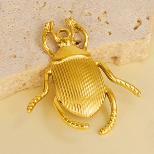 Detailed close-up of a golden stainless steel beetle pendant on a natural stone background