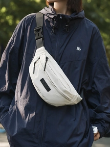 White nylon crossbody chest bag with adjustable strap worn by a model in outdoor street style