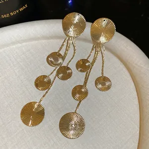 Golden drop tassel earrings with sunburst textured discs on a cream fabric tray
