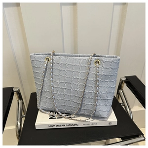 Detail of light blue textured tweed tote bag featuring gold chain and leather shoulder strap