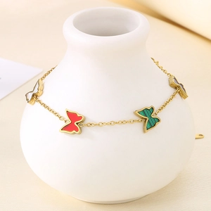 Close-up of a gold butterfly bracelet with colorful shell pendants on a white vase
