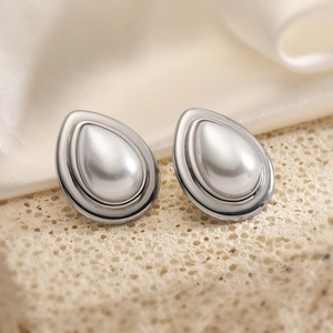 Waterdrop-shaped silver earrings with central pearl on beige stone and silk background