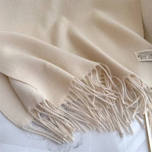 Close-up of beige cashmere-like scarf texture with fringe detail and white brand tag