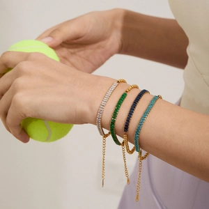 Stack of gold stainless steel bracelets with emerald, blue, and clear zircon gemstones