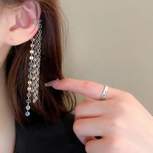 Detail of silver sequin tassel ear cuff and textured ring worn on female model