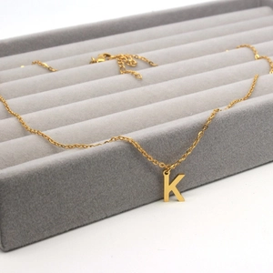 Detail of golden stainless steel letter K pendant necklace on grey velvet display tray