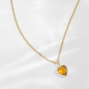 Close-up of heart-shaped amber gemstone pendant on a refined gold chain necklace