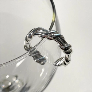 Detail shot of a silver twisted rope ring hanging on a clear glass edge with a white background