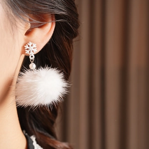 Close-up of white snowflake earring with pearl and fluffy faux fur pompom on model