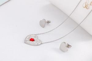 Detail of silver heart jewelry set featuring red stone pendant and matte stud earrings