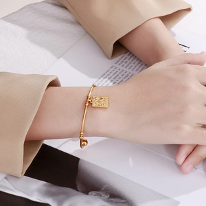 Detail of gold stainless steel beaded bracelet with a square pendant on a model