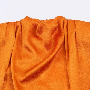 Detailed view of orange satin fabric with crinkle texture and soft natural luster