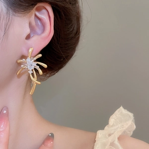 Close-up of elegant gold firework stud earrings with white zircons on female model