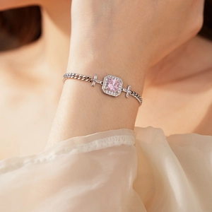 Detail of silver bracelet featuring pink emerald-cut stone and cross chain elements