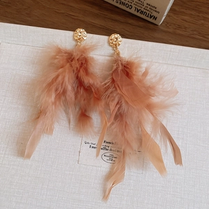 Dettaglio ravvicinato di orecchini boho con piume rosa mandorla e clip in lega dorata