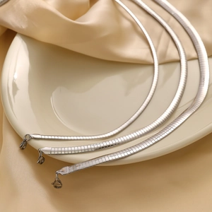 Three assorted silver stainless steel flat snake chain necklaces on a ceramic tray