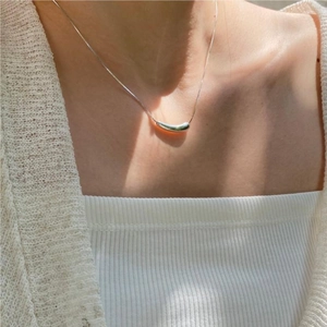Close-up of minimalist silver water drop pendant necklace on a female neck with soft shadows