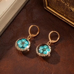 Macro detail of gold-plated earring with blue dried flower preserved in glass sphere