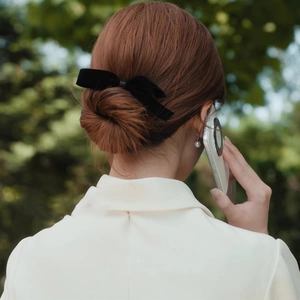 Elegant woman wearing black bow hair clip with white coat in park setting close-up