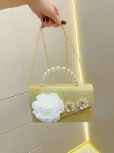 Detail of evening clutch with satin flower decor, pearl handle and gold glitter fabric