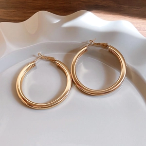 Close-up of glossy gold circular hoop earrings on a minimalist textured ceramic plate