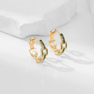 Detail showing gold-plated earrings with emerald green zircon stones on stone background
