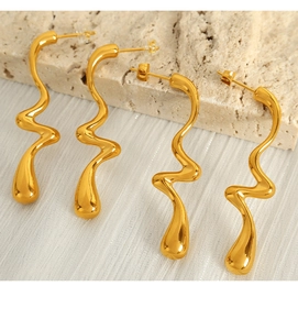 Detail of twisted gold wavy earrings with high-polish metallic finish on stone surface