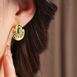 Gros plan d'une boucle d'oreille vintage dorée en U avec pierres bleues sur le mannequin