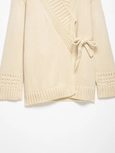 Detail of cream knit wrap cardigan showing hollow-out texture and side bow tie