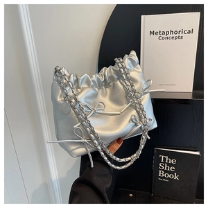 Detail of silver metallic PU bucket bag with bow decoration and chain strap held by hand