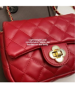 Detail of red quilted crossbody bag with golden clover clasp and metallic chain strap