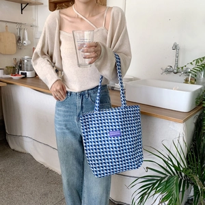 Detail of blue and white checkered canvas tote bag with purple label in lifestyle setting