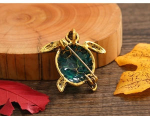 Detailed close-up of vintage sea turtle brooch with green enamel and gold finish on maple leaves