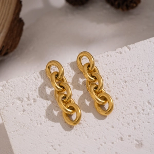 Détail de boucles d'oreilles chaîne dorées sur un support en pierre texturée blanche