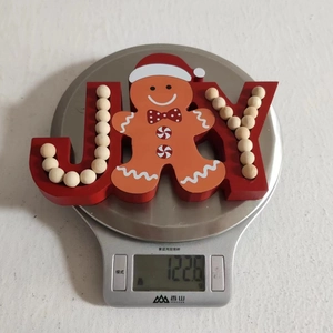 Close-up of JOY gingerbread man wooden Christmas ornament weighing 122.6g on a scale