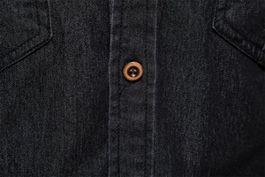 Macro detail of charcoal grey denim fabric featuring a brown button and precision stitching