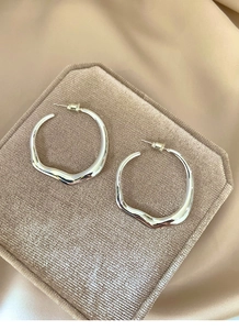 Close-up of silver irregular wavy hoop earrings on a beige velvet jewelry display