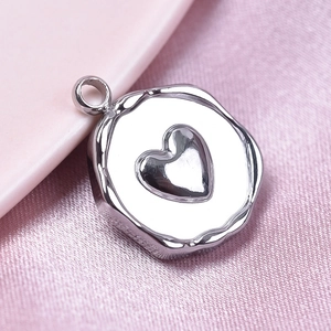 Macro shot of silver heart engraved irregular round pendant on pink silk background