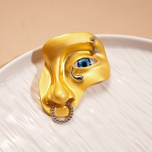 Détail d'une broche visage artistique avec œil bleu et anneau de nez en cristal