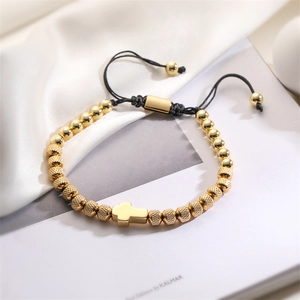 Close-up of golden beaded bracelet with cross charm on elegant white silk and book