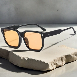 Detail of black square sunglasses with orange lenses and silver rivets on stone