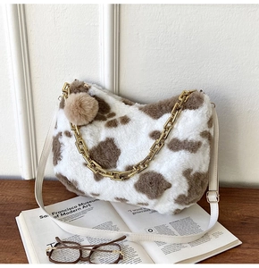 Detail of cow print faux fur tote bag with gold chain and plush ball charm on a book