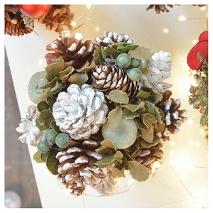 Close-up of a Christmas ornament featuring pine cones, green leaves, and silver berries
