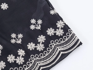 Detail of white floral embroidery and geometric lace hem on black fabric dress