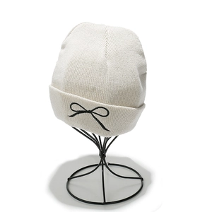 Detail of cream knit beanie featuring black embroidered bow on the folded cuff